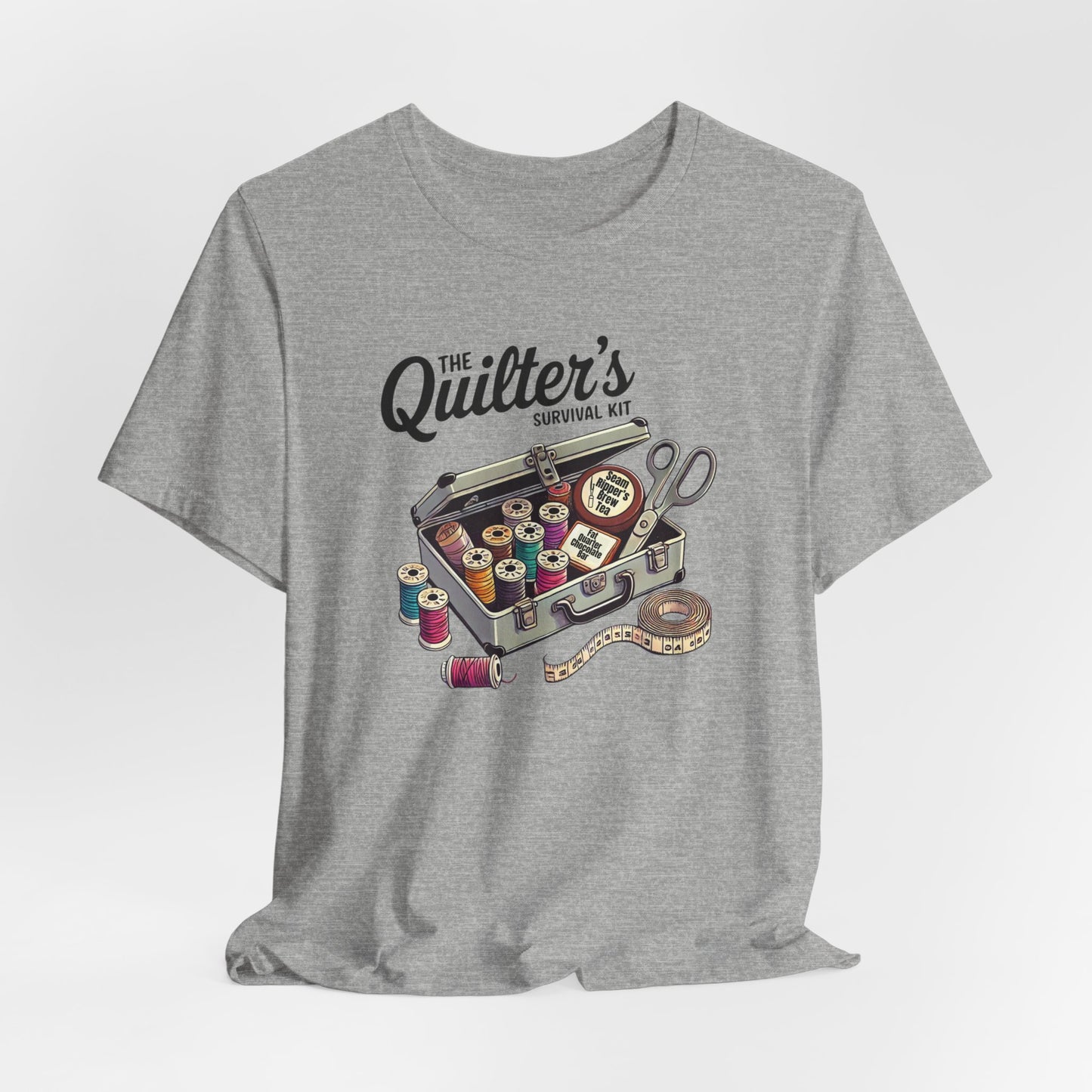 An Athletic Heather t-shirt featuring a whimsical illustration of a quilter’s survival kit with colorful thread spools, scissors, and a tape measure, perfect for sewing and quilting enthusiasts.