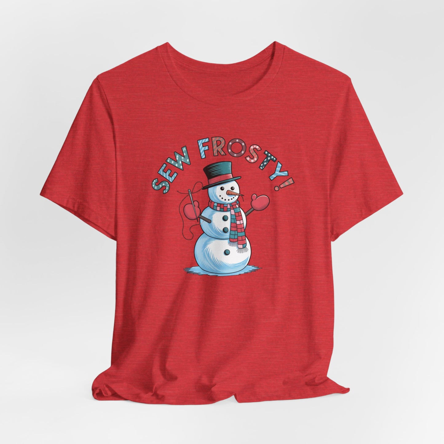 A Heather Red christmas quilting t-shirt featuring cheerful snowman design holding a sewing needle, with the phrase "Sew Frosty" in playful, winter-themed lettering. The snowman is wearing a scarf and mittens, ready for holiday sewing fun.