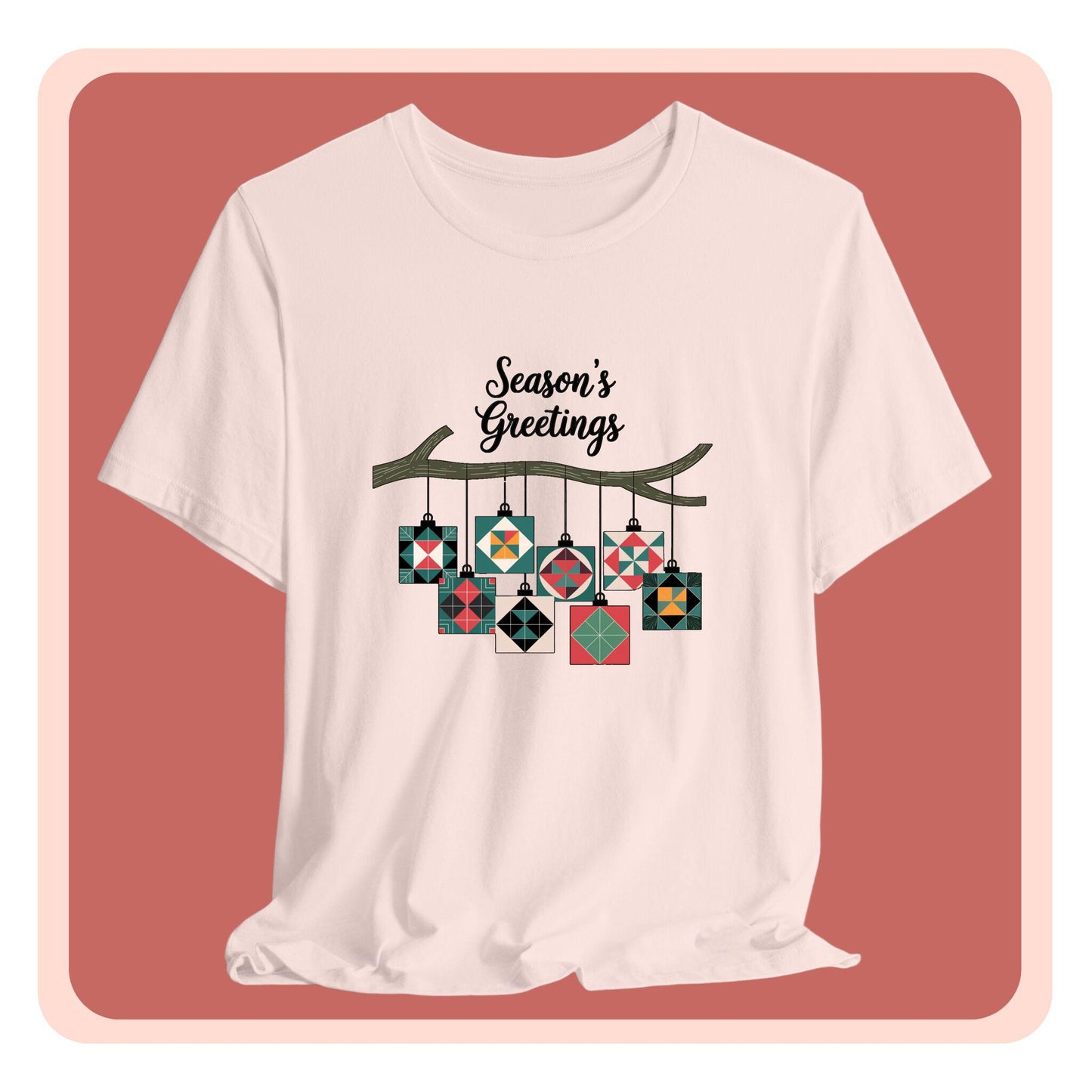 A christmas quilting t-shirt featuring quilt block ornaments hanging from a branch, featuring the phrase "Season's Greetings" above. The ornaments showcase various quilting patterns to highlight the holiday quilting theme.
