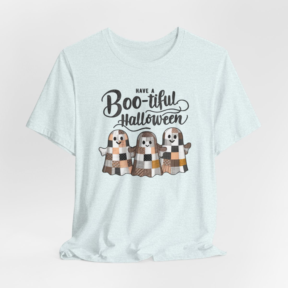 A Heather Ice Blue Halloween Quilting T-Shirt featuring three smiling patchwork ghosts made of various quilt patterns in autumn colors. Text reads "Have a Boo-tiful Halloween" in stylized lettering. Perfect for quilters who love Halloween.