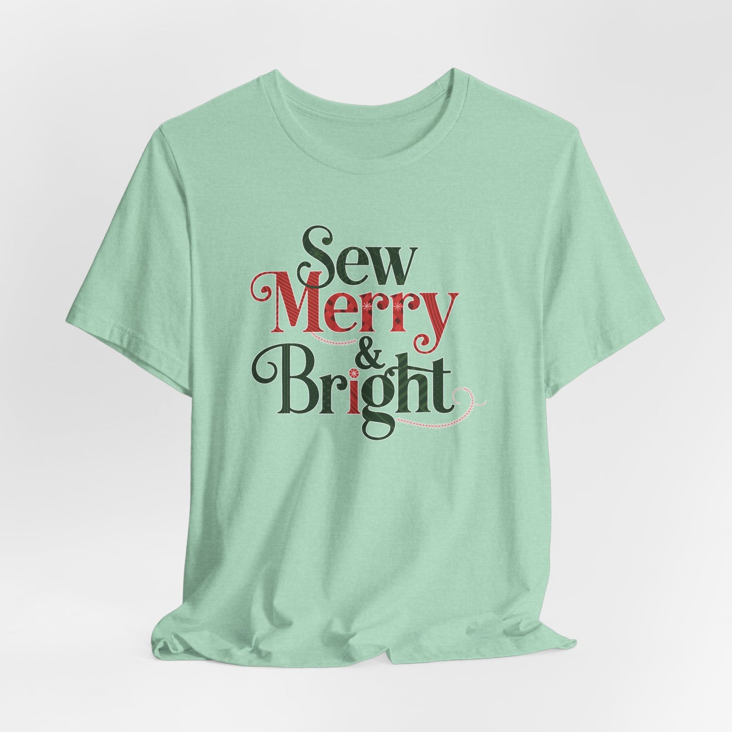 A Heather Mint t-shirt with the phrase "Sew Merry & Bright," incorporating sewing-inspired elements and holiday-themed accents, such as stitching lines and festive patterns.