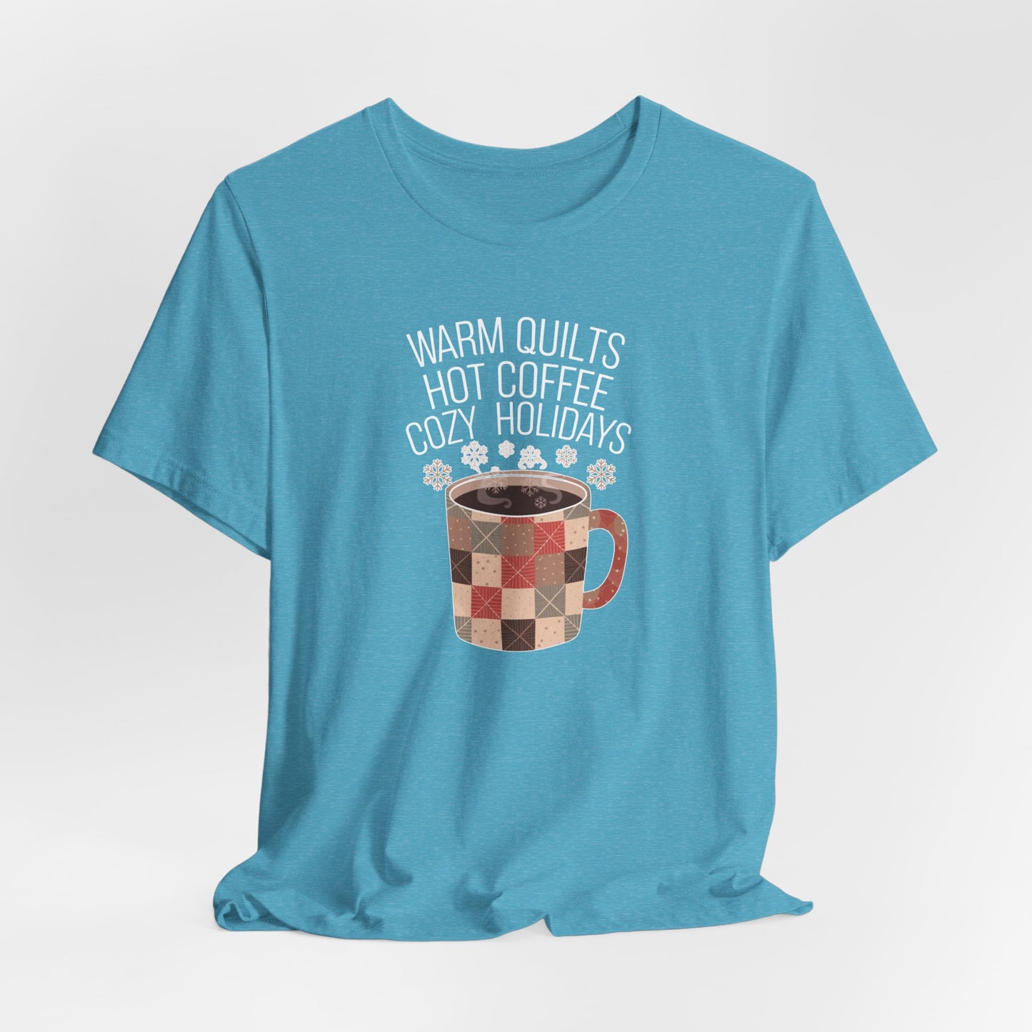 A Heather Aqua christmas quilting t-shirt featuring a cozy patchwork quilt-themed coffee mug, surrounded by snowflakes, with the phrase "Warm Quilts, Hot Coffee, Cozy Holidays" above the mug, celebrating the warmth of quilts and coffee during the holiday season.