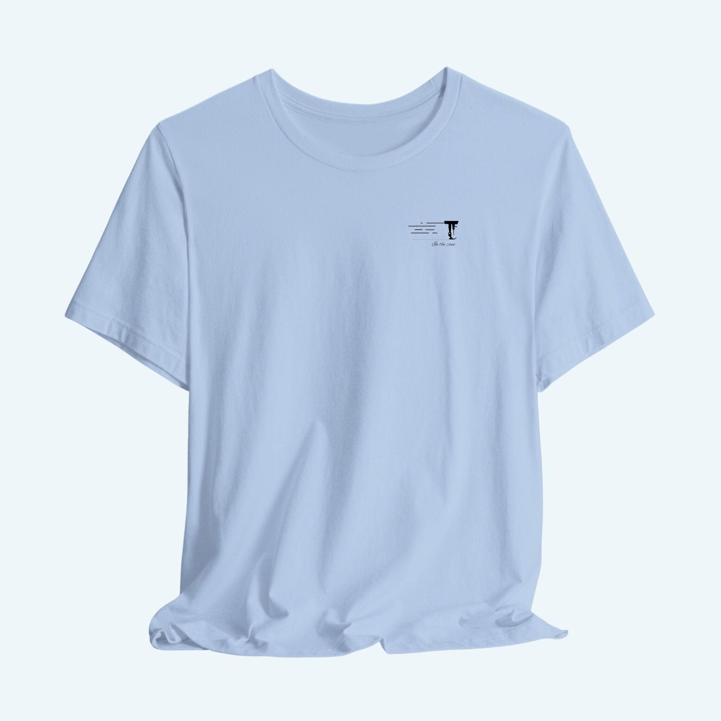 A T-shirt featuring a minimalist black silhouette of a sewing machine arm with motion lines. Below, the phrase "In the zone" is written in cursive script. The design conveys the focus and rhythm of quilting.