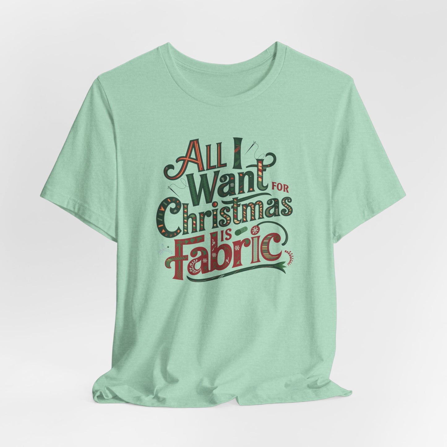 A Heather Mint festive quilting christmas T-shirt featuring the phrase "All I Want for Christmas is Fabric," with fun sewing and quilting accents like needles and threads swirling around the text.