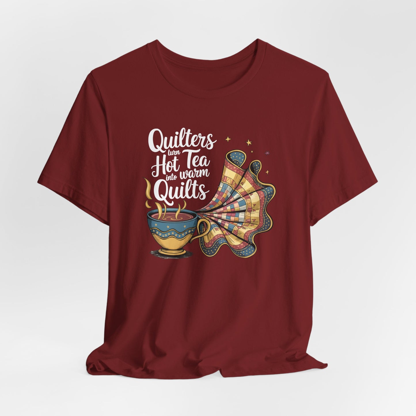 A Cardinal t-shirt with a whimsical design of a teacup transforming into a patchwork quilt, accompanied by the phrase 'Quilters turn hot tea into warm quilts.' Ideal for quilters and tea lovers