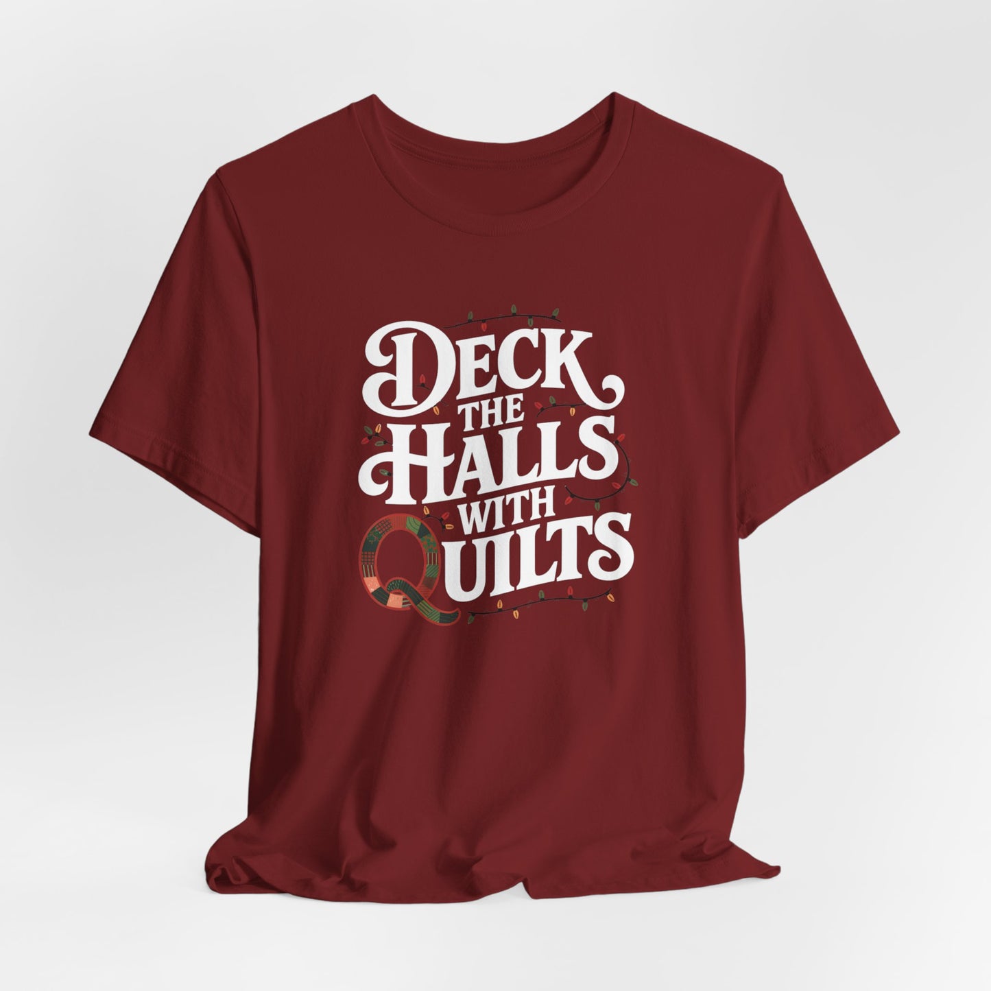 A Cardinal christmas quilting t-shirt featuring the phrase "Deck the Halls with Quilts," adorned with holiday lights and quilting-inspired elements, including a quilted 'Q' for a humorous touch.