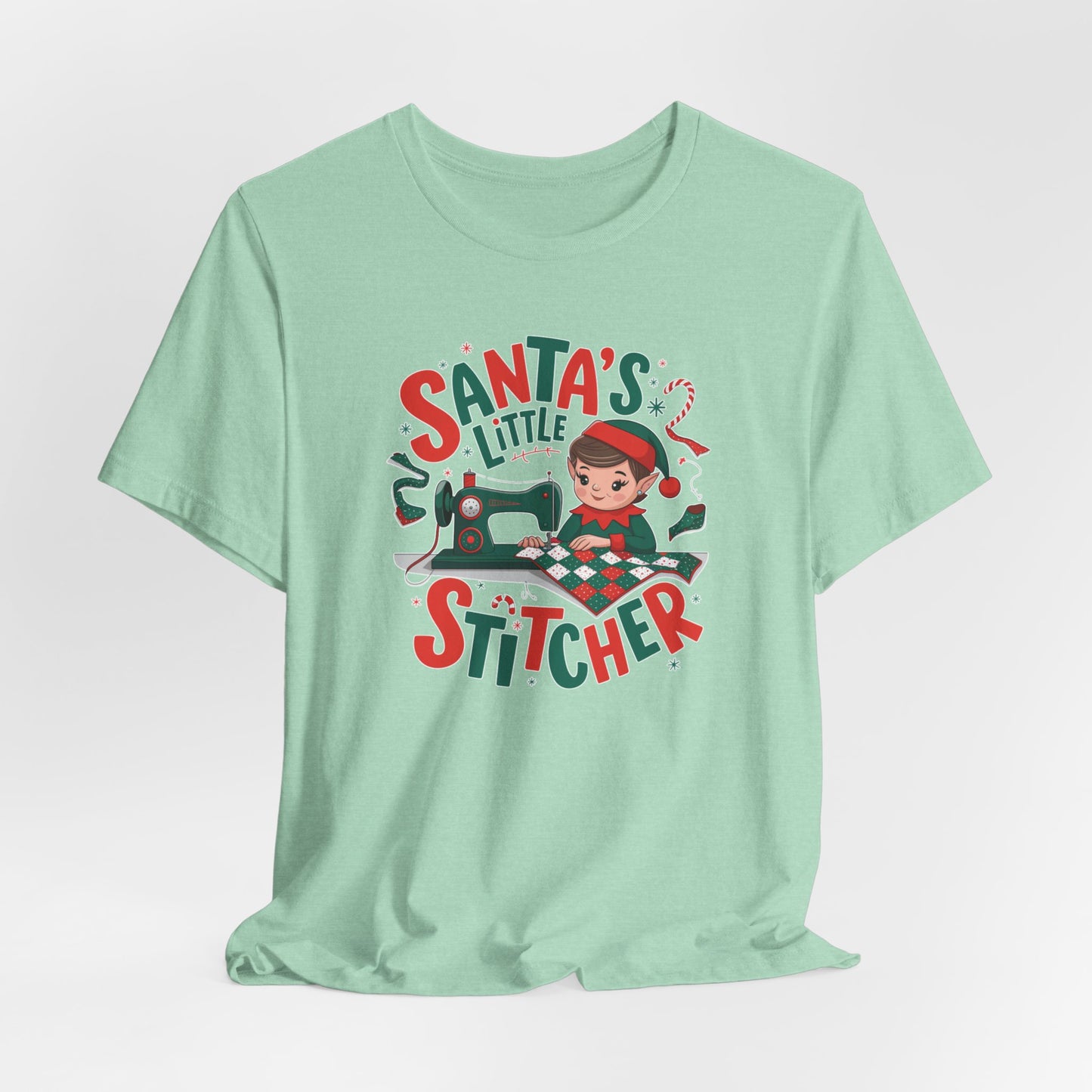 A Heather Mint christmas quilting t-shirt featuring an adorable elf is sewing a festive patchwork quilt on a sewing machine, surrounded by holiday-themed decorations, with the phrase "Santa's Little Stitcher" above and below the design.