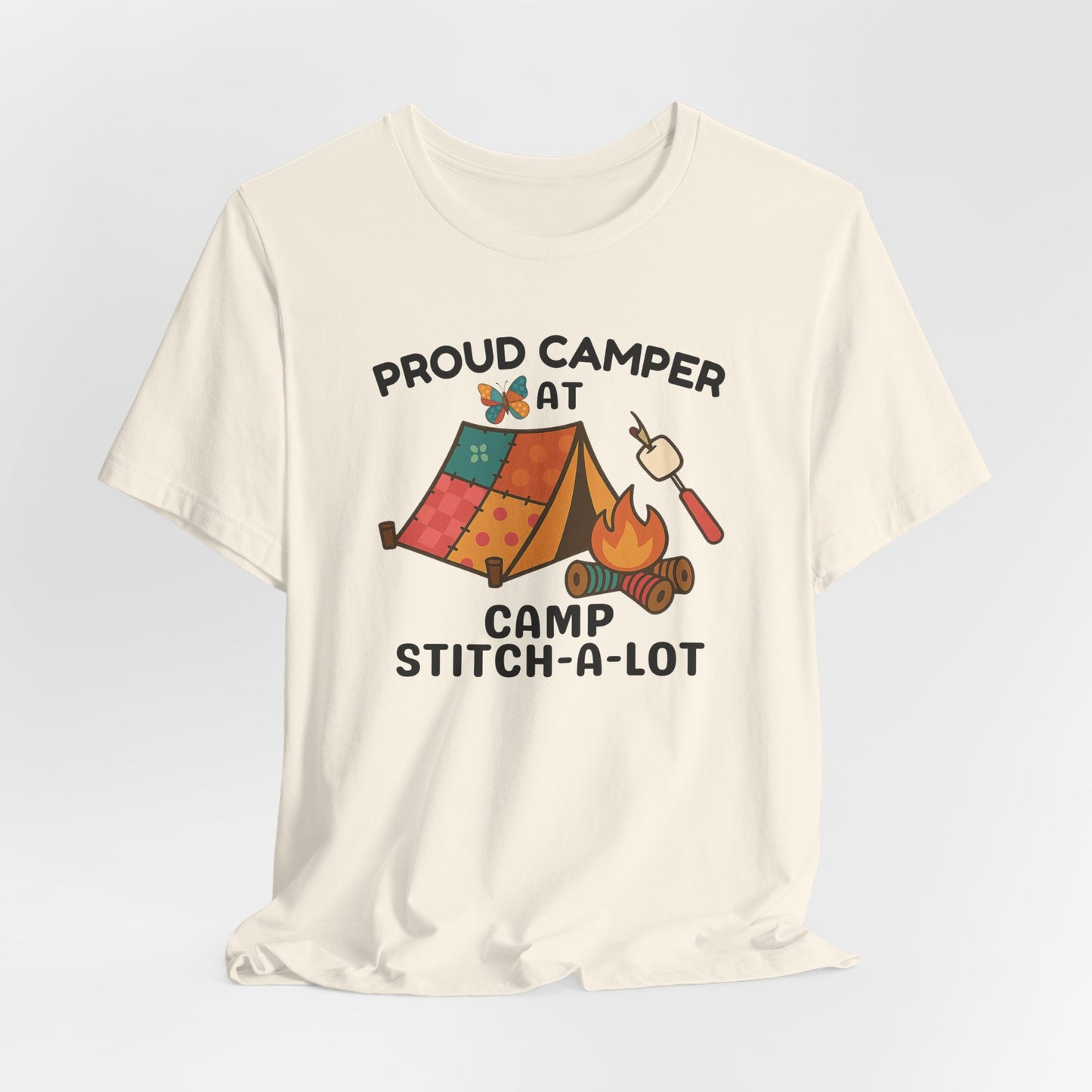 A A Natural t-shirt featuring a colorful design with a patchwork tent, thread spool campfire, marshmallow on a seam ripper stick, and a butterfly. Text reads "Proud Camper at Camp Stitch-a-Lot." Fun gift for quilting retreats.