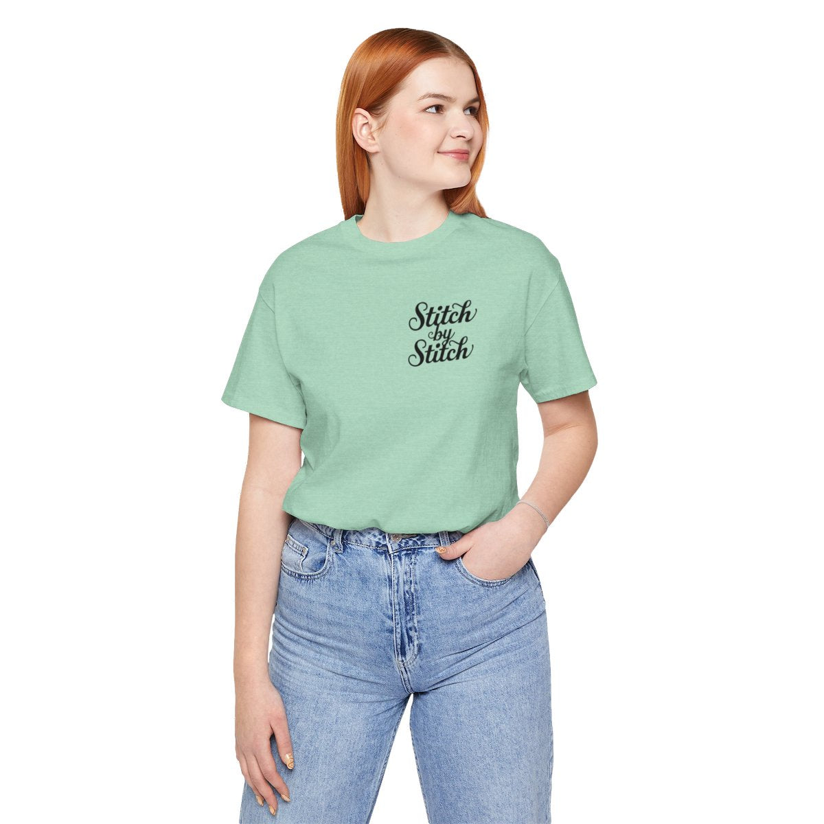 A Heather Mint T-Shirt featuring the phrase "Stitch by Stitch". The word "Stitch" is written twice in a flowing script font, while "by" is centered between them in a smaller, sans-serif font. The design has a clean, minimalist aesthetic.