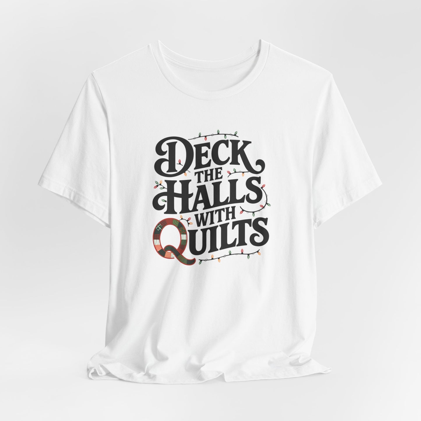 A White christmas quilting t-shirt featuring the phrase "Deck the Halls with Quilts," adorned with holiday lights and quilting-inspired elements, including a quilted 'Q' for a humorous touch.