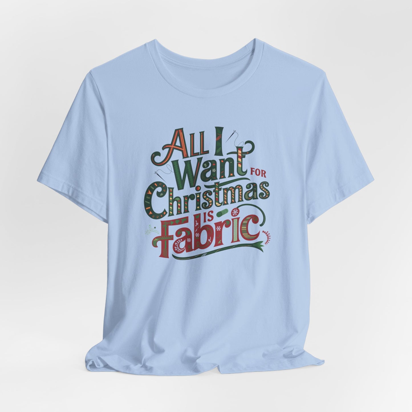 A Baby Blue festive quilting christmas T-shirt featuring the phrase "All I Want for Christmas is Fabric," with fun sewing and quilting accents like needles and threads swirling around the text.