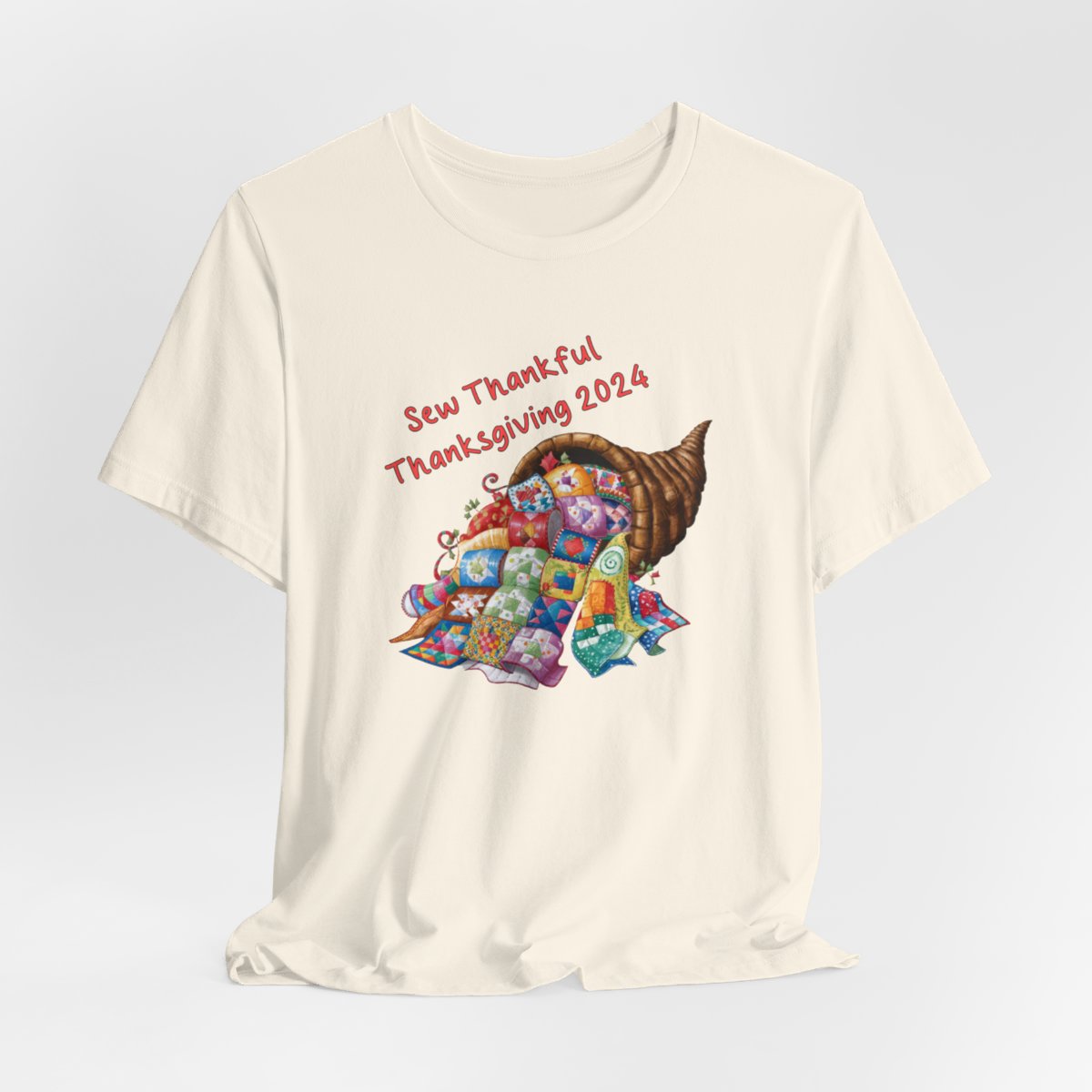 A Natural thanksgiving quilting t-shirt featuring a colorful quilted cornucopia overflowing with various quilt patterns and designs. Text reads "Sew Thankful Thanksgiving 2024" in red. Vibrant illustration combines quilting motifs with Thanksgiving imagery.