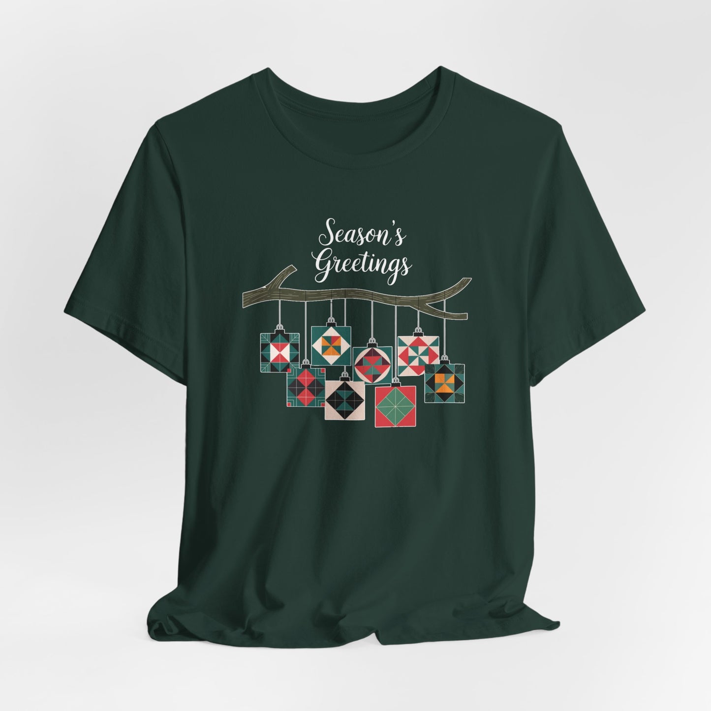 A Forest christmas quilting t-shirt featuring quilt block ornaments hanging from a branch, featuring the phrase "Season's Greetings" above. The ornaments showcase various quilting patterns to highlight the holiday quilting theme.
