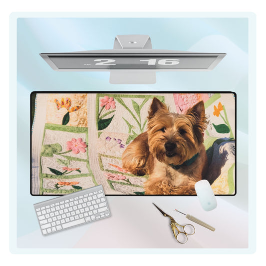 A quilting inspired Desk pad design showing a terrier puppy sitting on a colorful spring-themed quilt with various flower patterns. The quilt features pink, yellow, and green patches with intricate floral designs, creating a cheerful and vibrant workspace accessory. Perfect gift for quilters.
