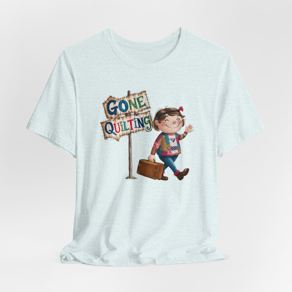 A Heather Ice Bluefun quilting T-Shirt with a cartoon illustration of a smiling girl wearing a patchwork jacket, carrying a suitcase next to a wooden sign that reads "Gone Quilting" in colorful letters.