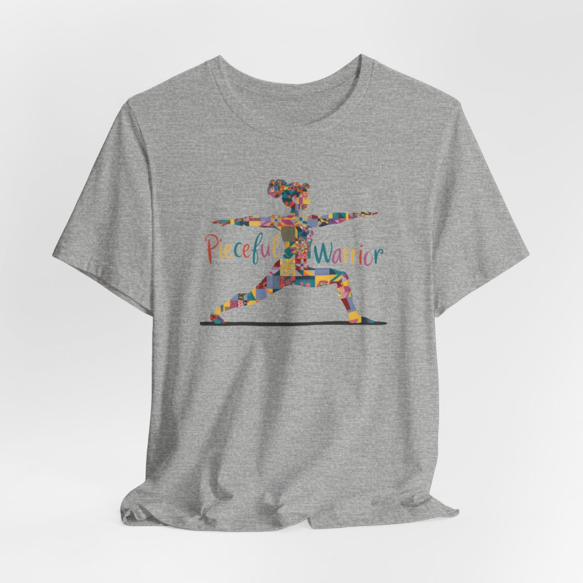 An Athletic Heather Tee featuring a colorful patchwork silhouette of woman in yoga warrior pose. Text reads "Pieceful Warrior" in multicolored lettering.