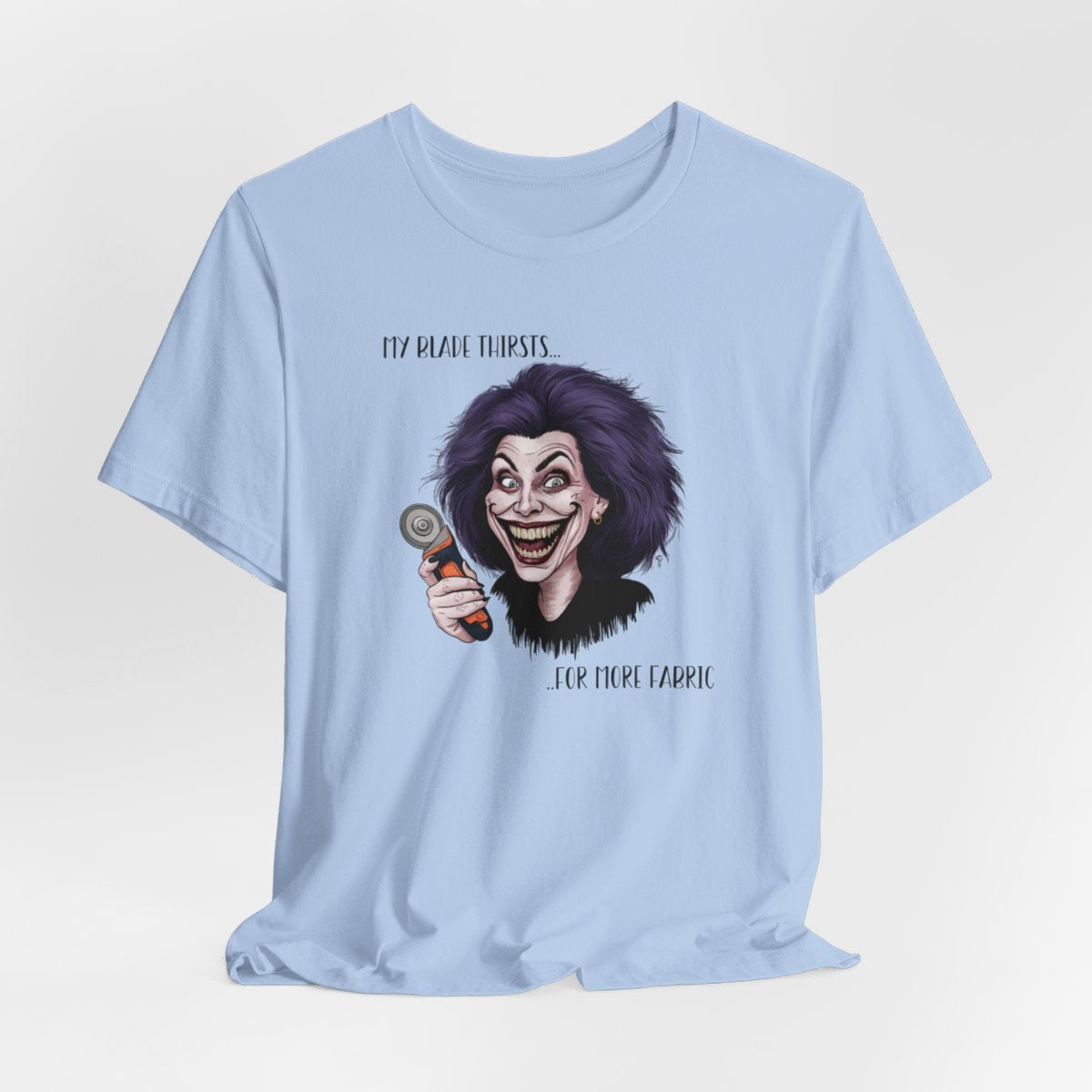 A Baby Blue T-shirt showing a cartoonish character with wild purple hair and an exaggerated grin, holding a rotary cutter. Text reads "My blade thirsts... for more fabric", humorously depicting a quilter's endless desire for new materials.