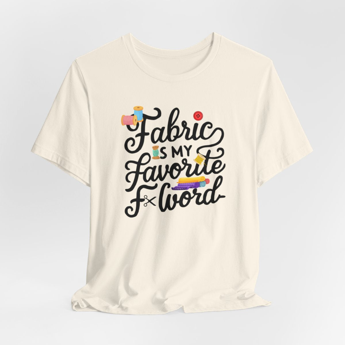 A Natural T-Shirt with the phrase Fabric is My Favorite F-Word in a bold font with thread, buttons, and fabric bolts