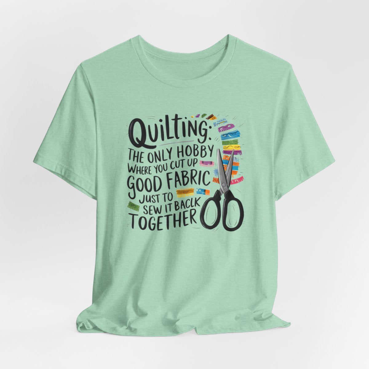 A Heather Mint Quilting-themed T-Shirt with text "Quilting: The Only Hobby Where You Cut Up Good Fabric Just to Sew it Back Together" surrounded by colorful fabric scraps and scissors.