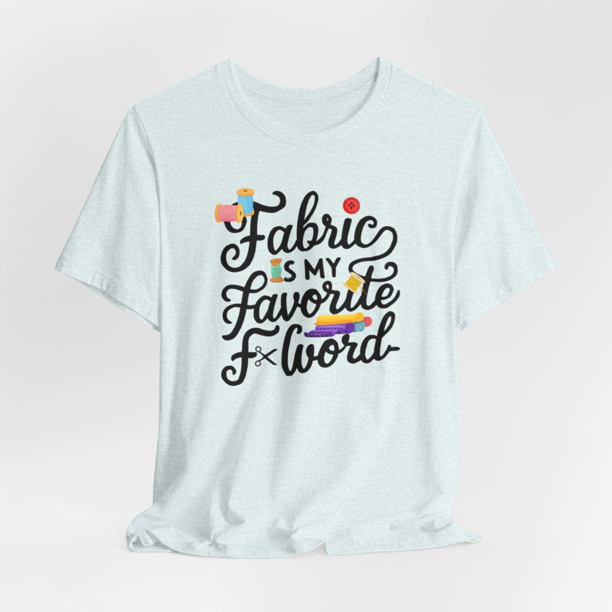 A Heather Ice Blue T-Shirt with the phrase Fabric is My Favorite F-Word in a bold font with thread, buttons, and fabric bolts