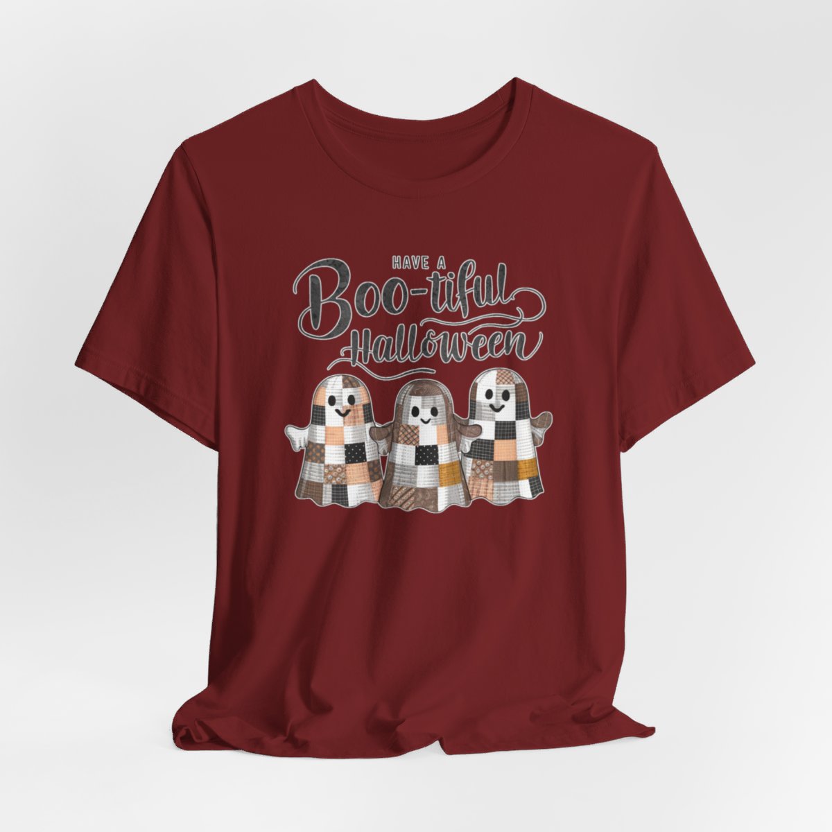 A Halloween Quilting T-Shirt featuring three smiling patchwork ghosts made of various quilt patterns in autumn colors. Text reads "Have a Boo-tiful Halloween" in stylized lettering. Perfect for quilters who love Halloween.