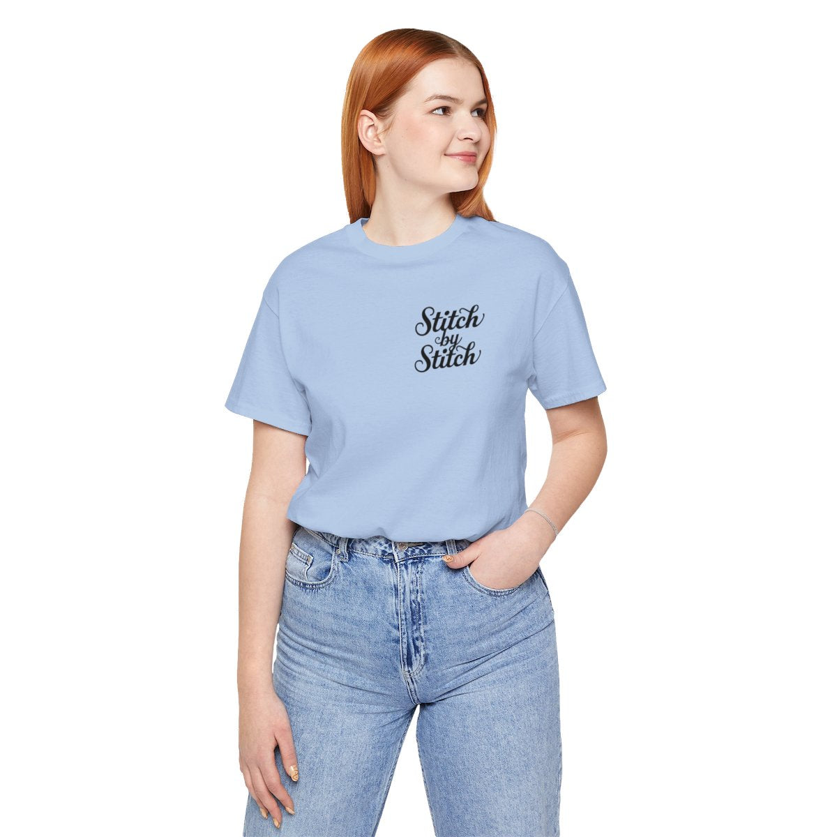 A Baby Blue T-Shirt featuring the phrase "Stitch by Stitch". The word "Stitch" is written twice in a flowing script font, while "by" is centered between them in a smaller, sans-serif font. The design has a clean, minimalist aesthetic.