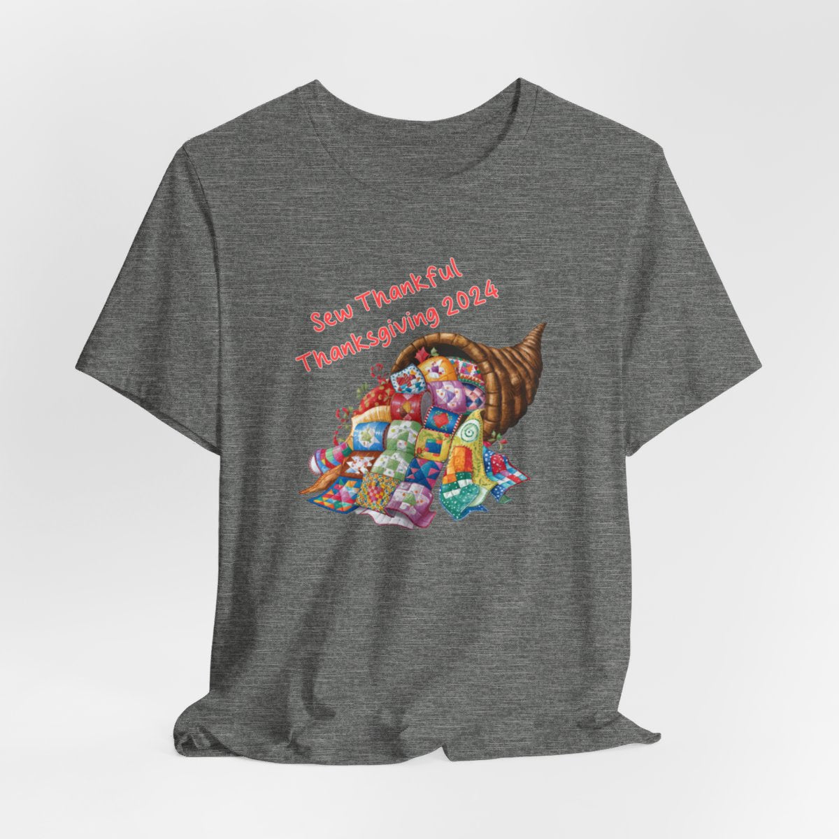 A Deep Heather thanksgiving quilting t-shirt featuring a colorful quilted cornucopia overflowing with various quilt patterns and designs. Text reads "Sew Thankful Thanksgiving 2024" in red. Vibrant illustration combines quilting motifs with Thanksgiving imagery.