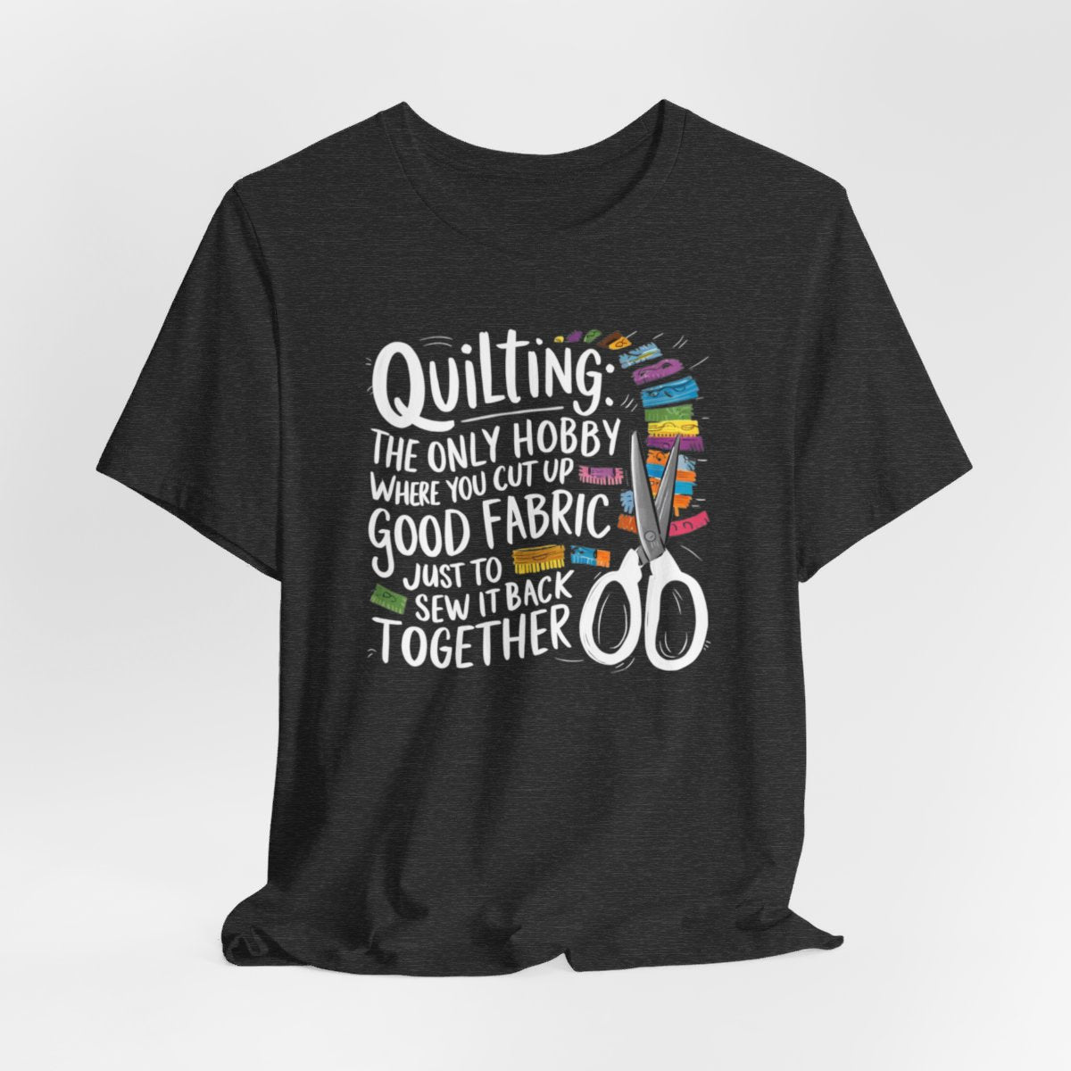 A Dark Grey Heather Quilting-themed T-Shirt with text "Quilting: The Only Hobby Where You Cut Up Good Fabric Just to Sew it Back Together" surrounded by colorful fabric scraps and scissors.
