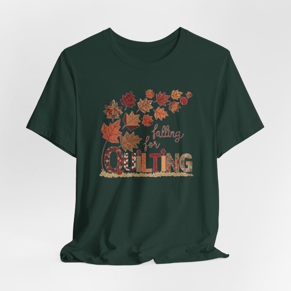 A Forest thanksgiving quilting t-shirt featuring autumn leaves with various quilting patterns inside. Text reads "falling for QUILTING" with letters in patchwork style. Warm fall colors and quilting motifs combine in a seasonal design.