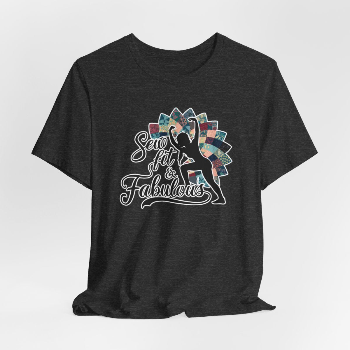 A Dark Grey Heather T-Shirt featuring a black silhouette of woman with raised arms against colorful patchwork background. Text reads "Sew fit & Fabulous" in stylized script.