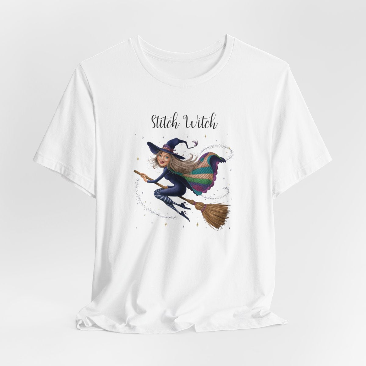 A White Halloween Quilting T-Shirt featuring a witch riding broomstick on t-shirt design. Colorful patchwork quilt cape with various patterns. Sparkling magic and stars. Text reads "Stitch Witch". Ideal for quilters who enjoy magical themes.