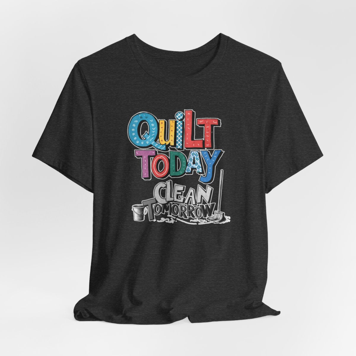 A Dark Grey Heather funny quilting T-Shirt with the phrase Quilt Today, Clean Tomorrow in a bold and cheerful font with a broom off to the side