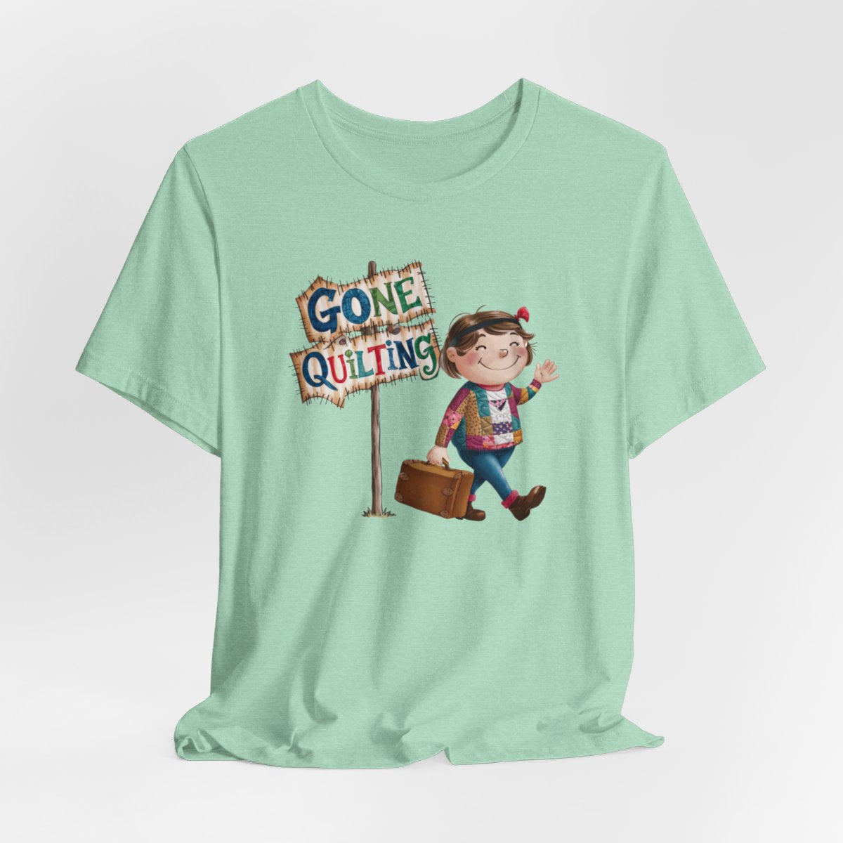 A Heather Mintfun quilting T-Shirt with a cartoon illustration of a smiling girl wearing a patchwork jacket, carrying a suitcase next to a wooden sign that reads "Gone Quilting" in colorful letters.