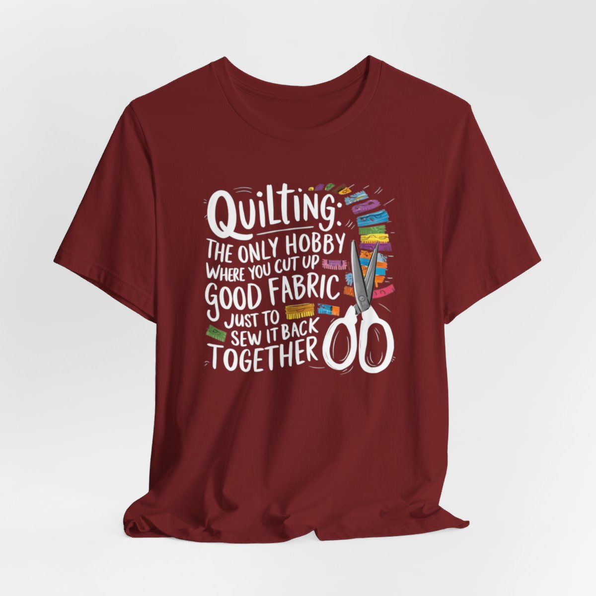 A Cardinal Quilting-themed T-Shirt with text "Quilting: The Only Hobby Where You Cut Up Good Fabric Just to Sew it Back Together" surrounded by colorful fabric scraps and scissors.