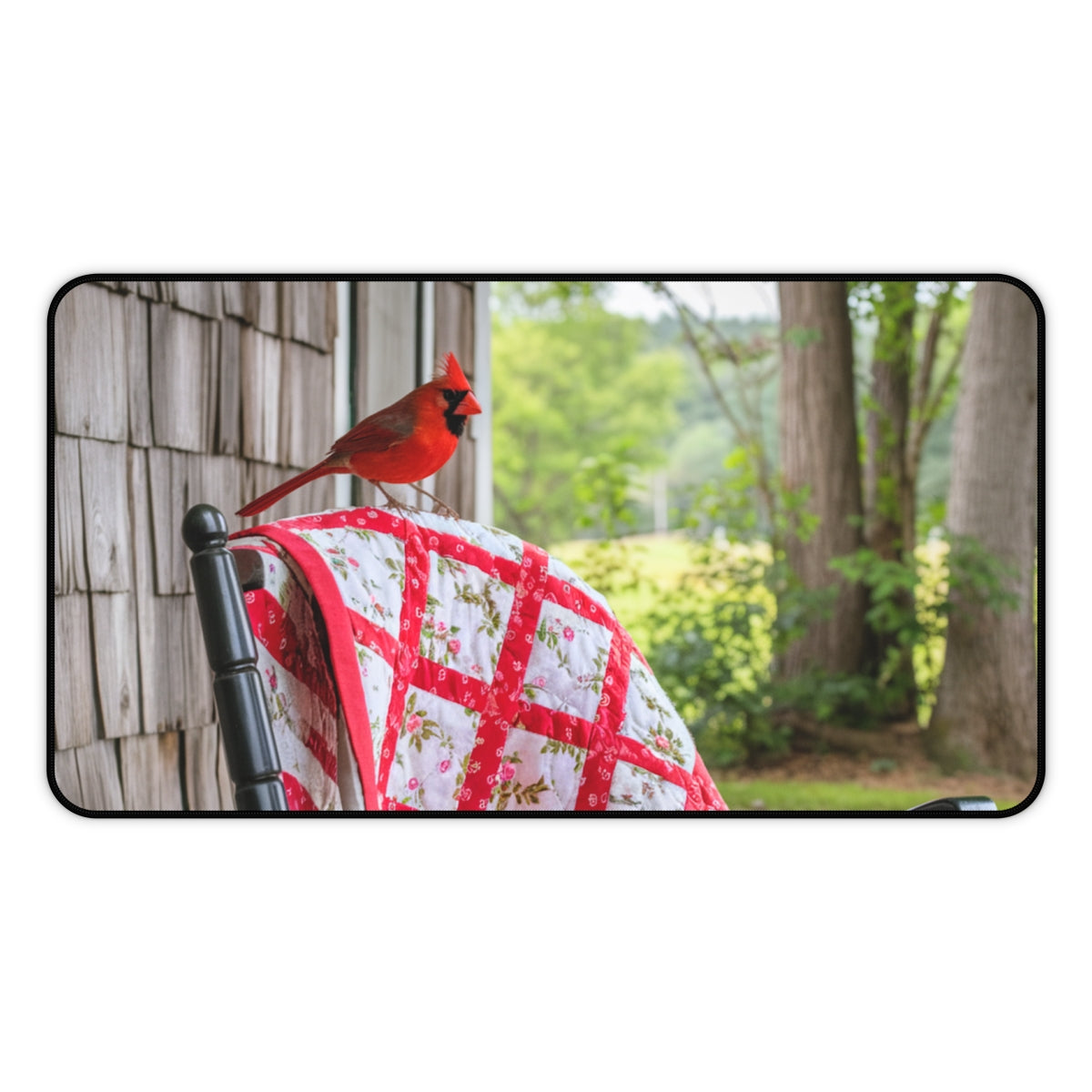 A quilting inspired Desk pad featuring a red cardinal perched on a folded red and white quilt with a floral pattern. The quilt is draped over a wooden chair on a porch, with lush green foliage in the background. Perfect gift for quilters.