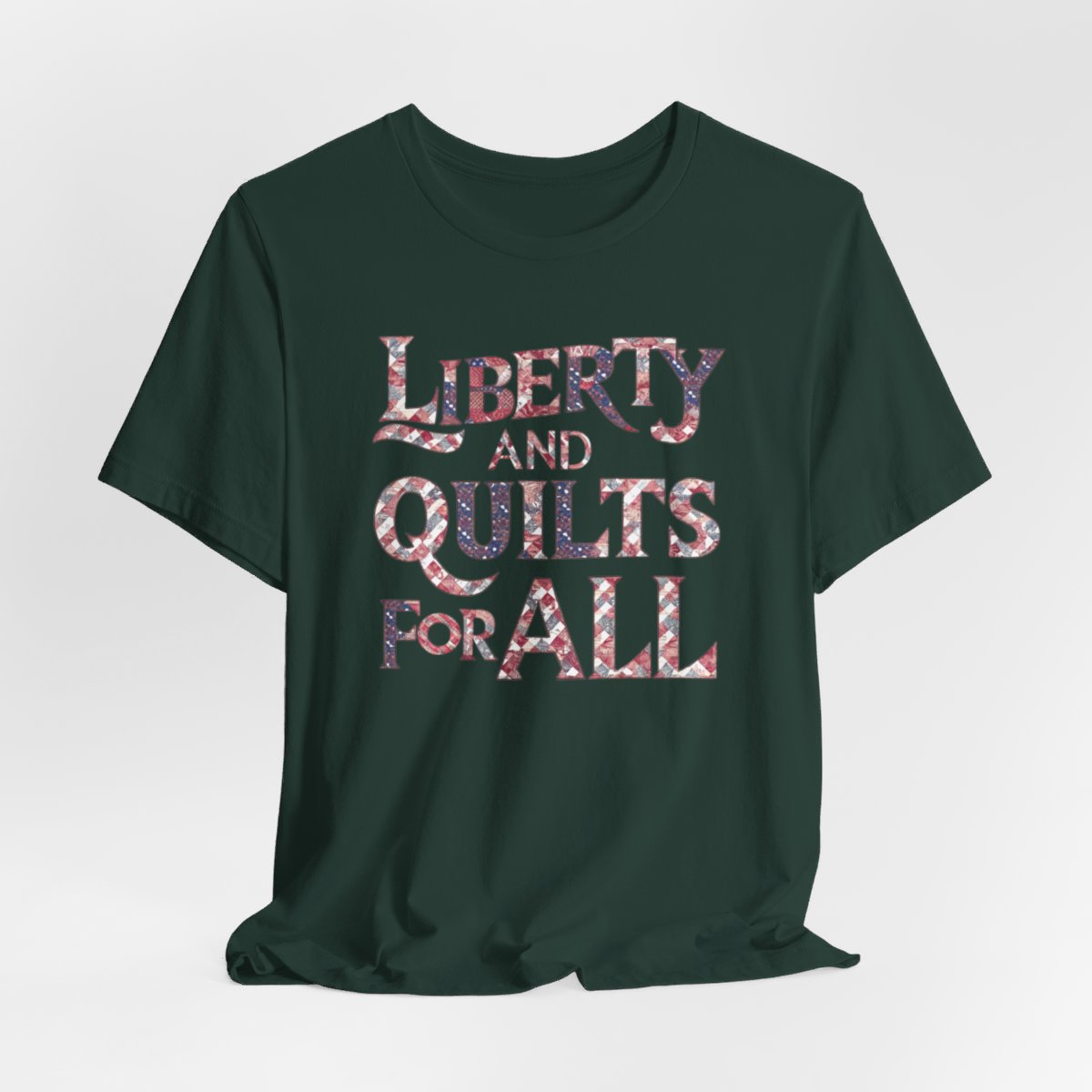A Forest T-shirt featuring text "LIBERTY AND QUILTS FOR ALL" in large decorative letters filled with various quilt patterns in red, white, and blue.