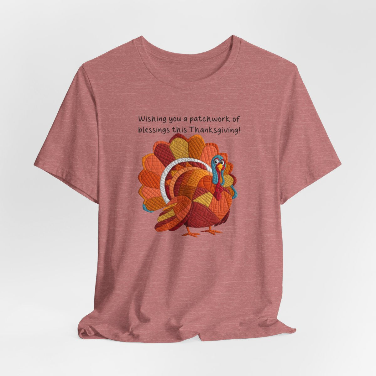 A Heather Mauve thanksgiving quilting t-shirt featuring a quilted patchwork turkey in autumn colors with text "Wishing you a patchwork of blessings this Thanksgiving!" Turkey features various quilt patterns and textures in shades of orange, red, yellow, and blue. Whimsical, crafty holiday design perfect for quilting enthusiasts.