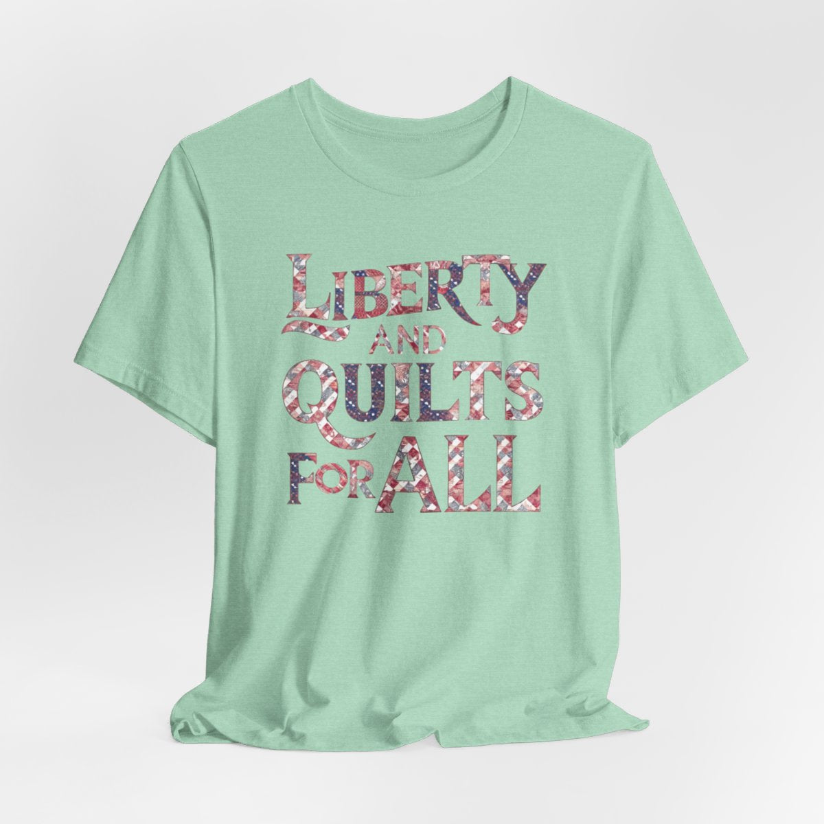 A Heather Mint T-shirt featuring text "LIBERTY AND QUILTS FOR ALL" in large decorative letters filled with various quilt patterns in red, white, and blue.