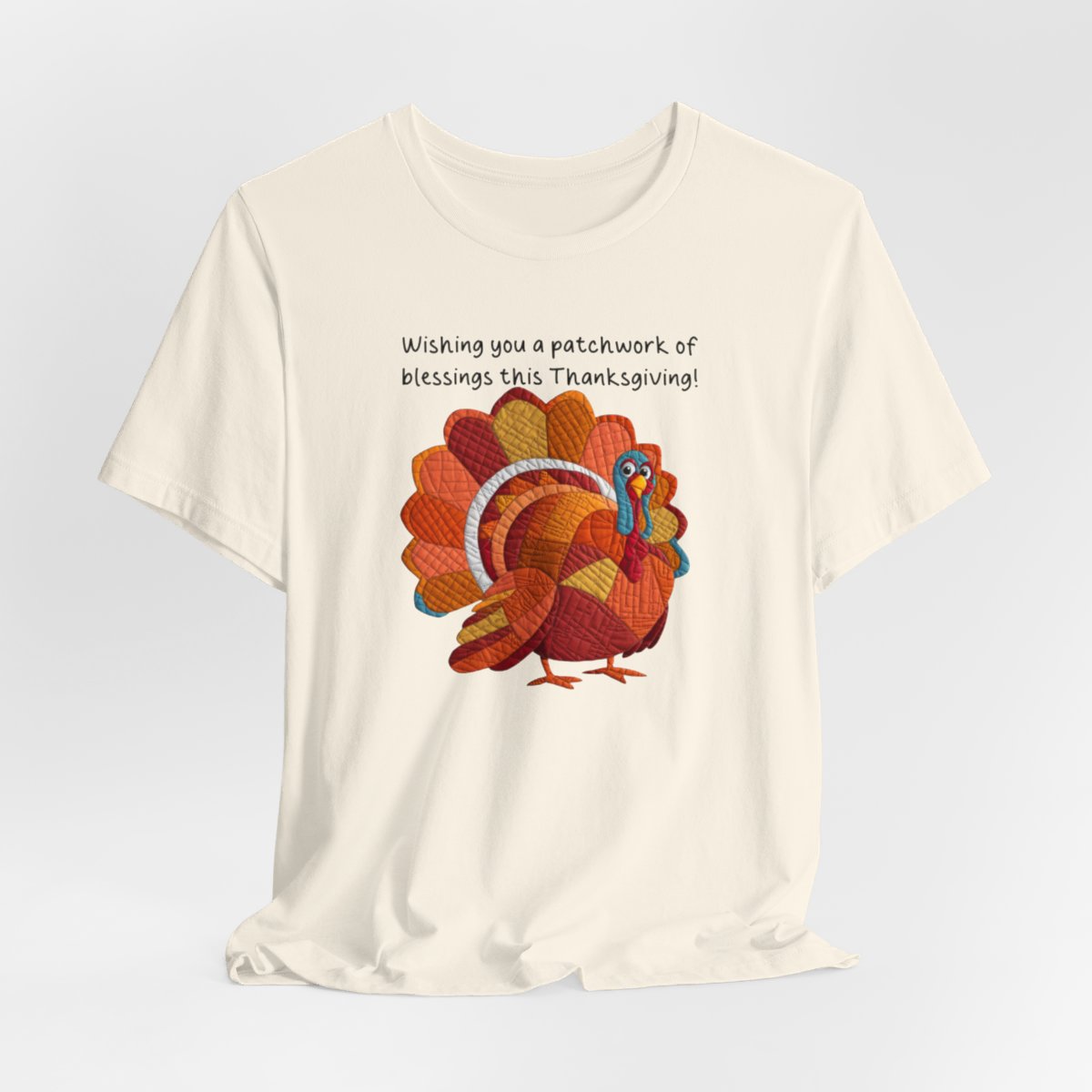 A Natural thanksgiving quilting t-shirt featuring a quilted patchwork turkey in autumn colors with text "Wishing you a patchwork of blessings this Thanksgiving!" Turkey features various quilt patterns and textures in shades of orange, red, yellow, and blue. Whimsical, crafty holiday design perfect for quilting enthusiasts.