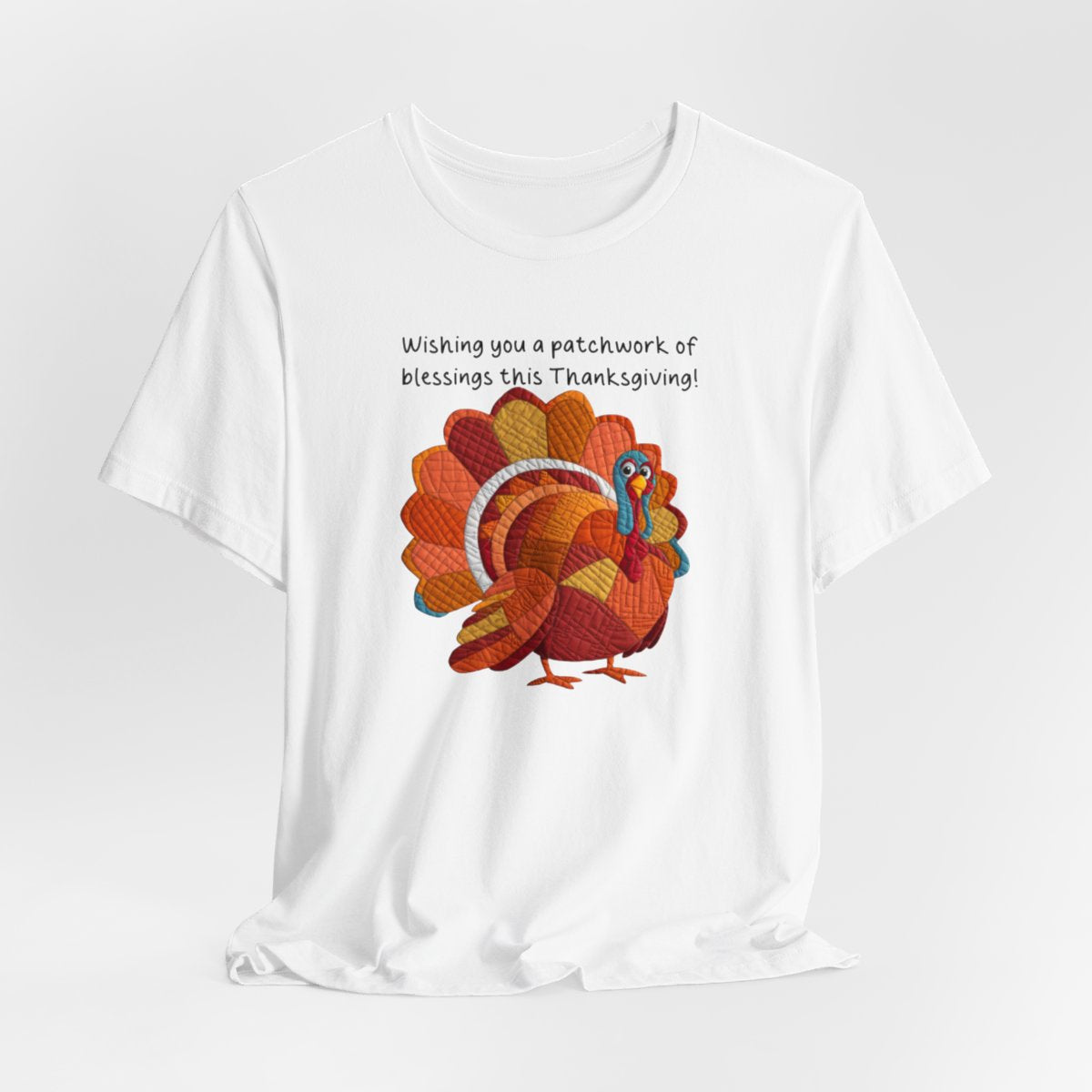 A White thanksgiving quilting t-shirt featuring a quilted patchwork turkey in autumn colors with text "Wishing you a patchwork of blessings this Thanksgiving!" Turkey features various quilt patterns and textures in shades of orange, red, yellow, and blue. Whimsical, crafty holiday design perfect for quilting enthusiasts.