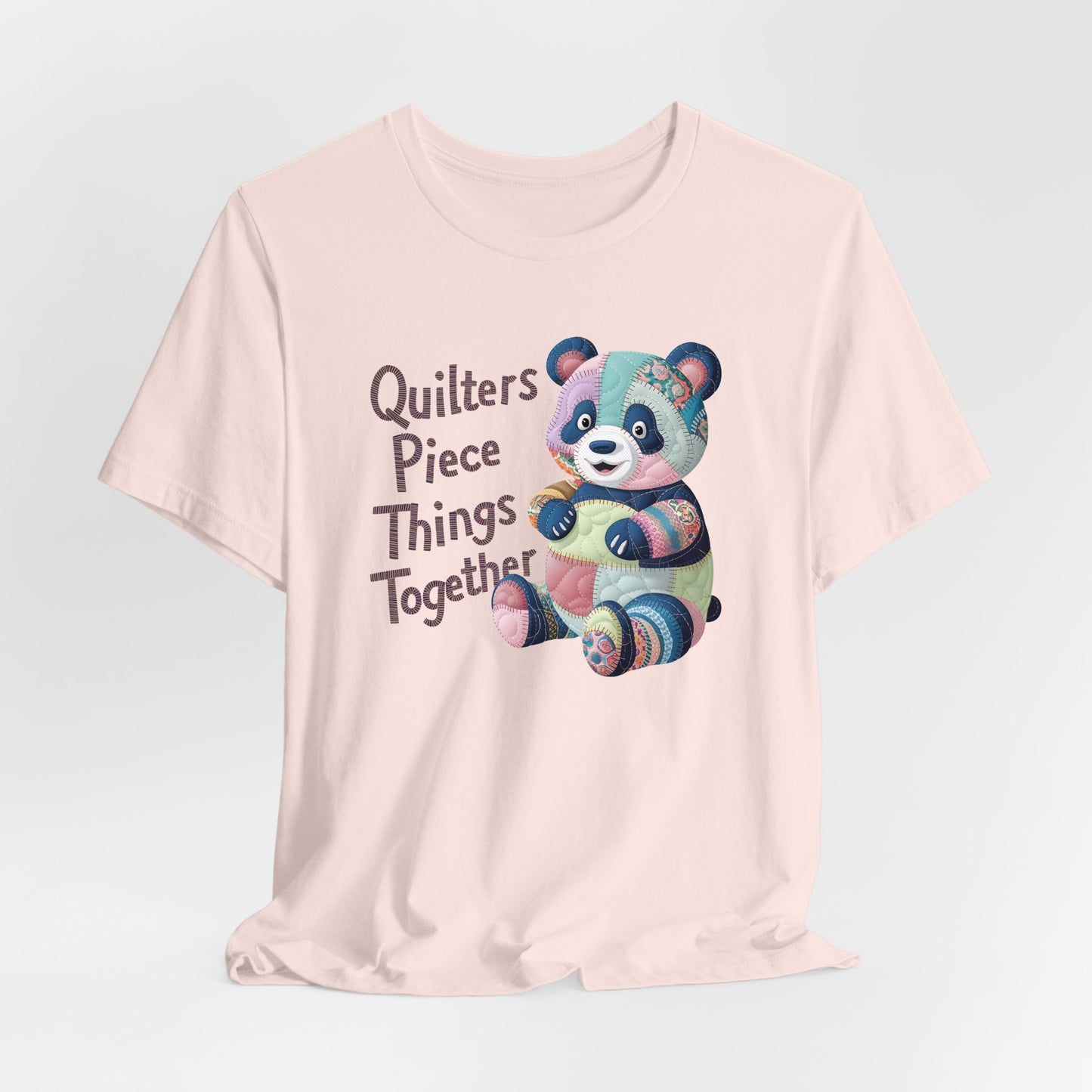 A Soft Pink Short Sleeve T-Shirt with a patchwork panda with "Quilters Piece Things Together" text in a whimsical style