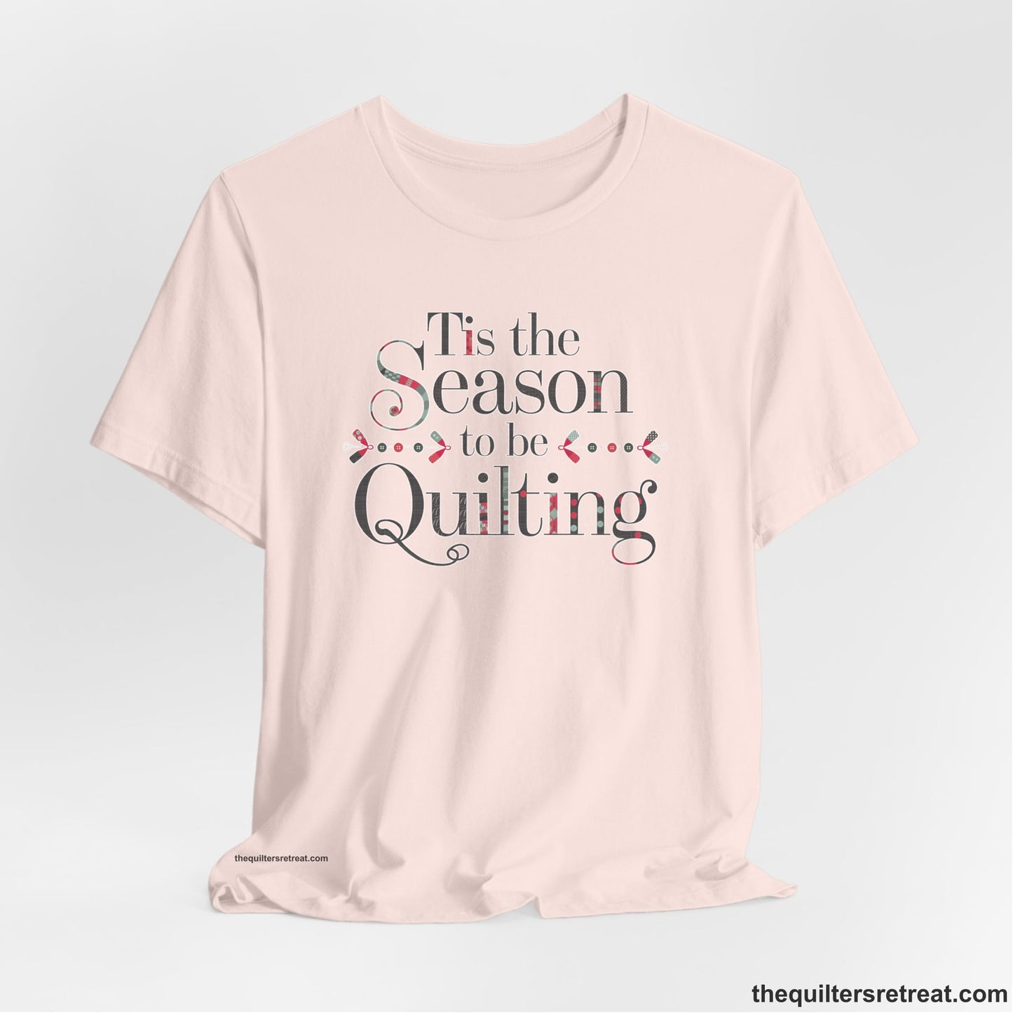 A Soft Pink Short Sleeve T-Shirt with a tis the season to be quilting text with festive patchwork pattern in a cheerful style
