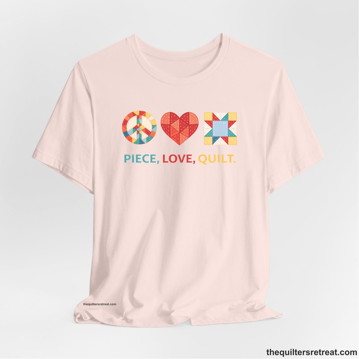 A Soft Pink Short Sleeve T-Shirt with a Colorful quilt patterns, "PIECE, LOVE, QUILT." text, whimsical style.