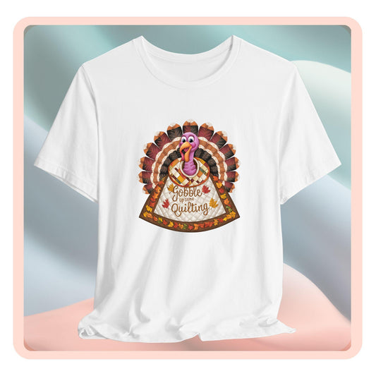 A thanksgiving  quilting t-shirt featuring a quilted turkey design with colorful patchwork feathers and body. Text on turkey reads "Gobble up some Quilting" surrounded by fall leaves. Combines Thanksgiving imagery with quilting motifs in a whimsical illustration.