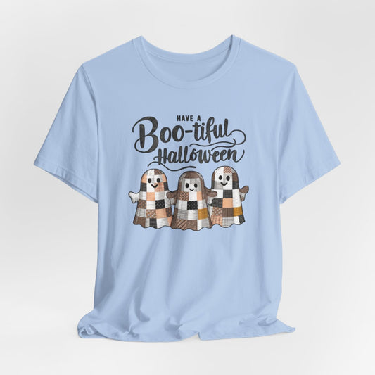 A Baby Blue Halloween Quilting T-Shirt featuring three smiling patchwork ghosts made of various quilt patterns in autumn colors. Text reads "Have a Boo-tiful Halloween" in stylized lettering. Perfect for quilters who love Halloween.