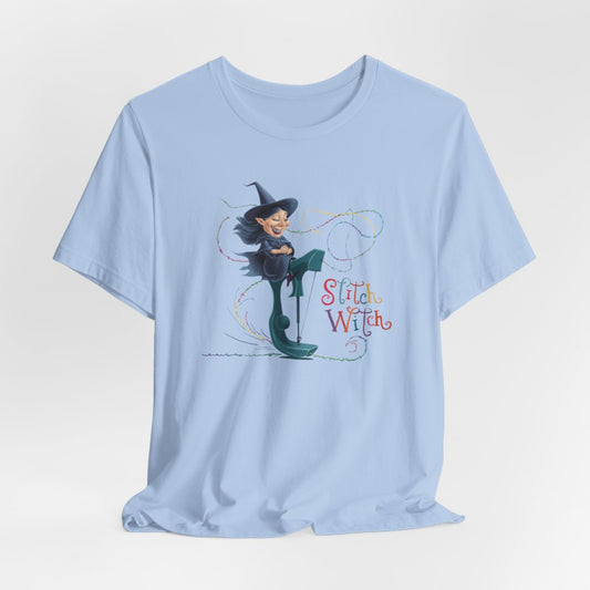 A Baby Blue T-shirt with a cartoon illustration of a smiling witch with pointed hat riding a teal sewing machine. Colorful stitches swirl around her in the air. Text reads "Stitch Witch" in playful, multicolored letters.