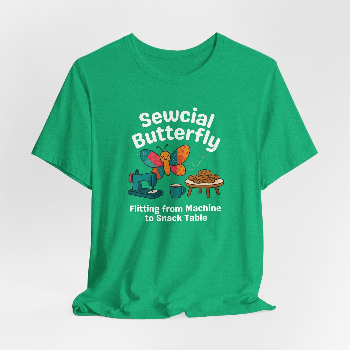 A A Heather Kelly t-shirt with a colorful design showing a patchwork butterfly flying between a sewing machine and a table of cookies. Text reads “Sewcial Butterfly – Flitting from Machine to Snack Table.” Funny gift for quilters