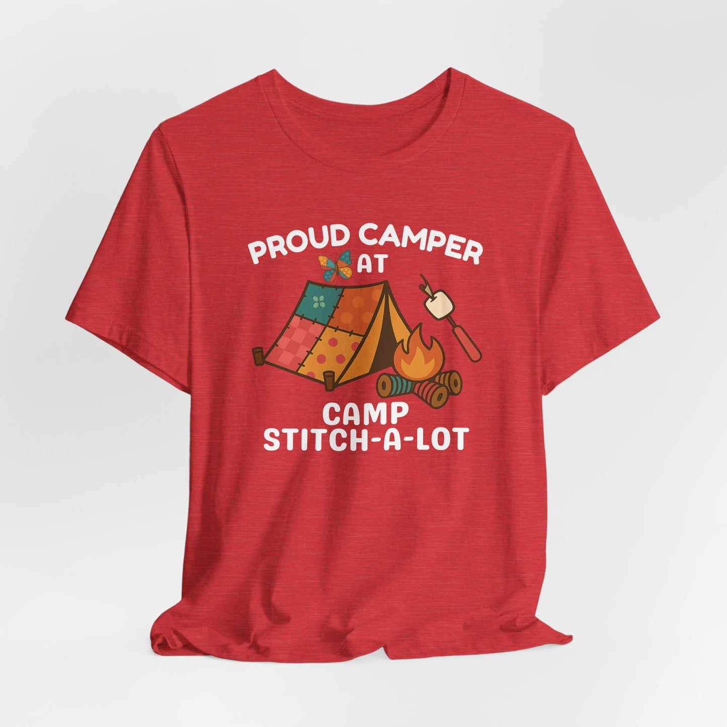 A A Heather Red t-shirt featuring a colorful design with a patchwork tent, thread spool campfire, marshmallow on a seam ripper stick, and a butterfly. Text reads "Proud Camper at Camp Stitch-a-Lot." Fun gift for quilting retreats.