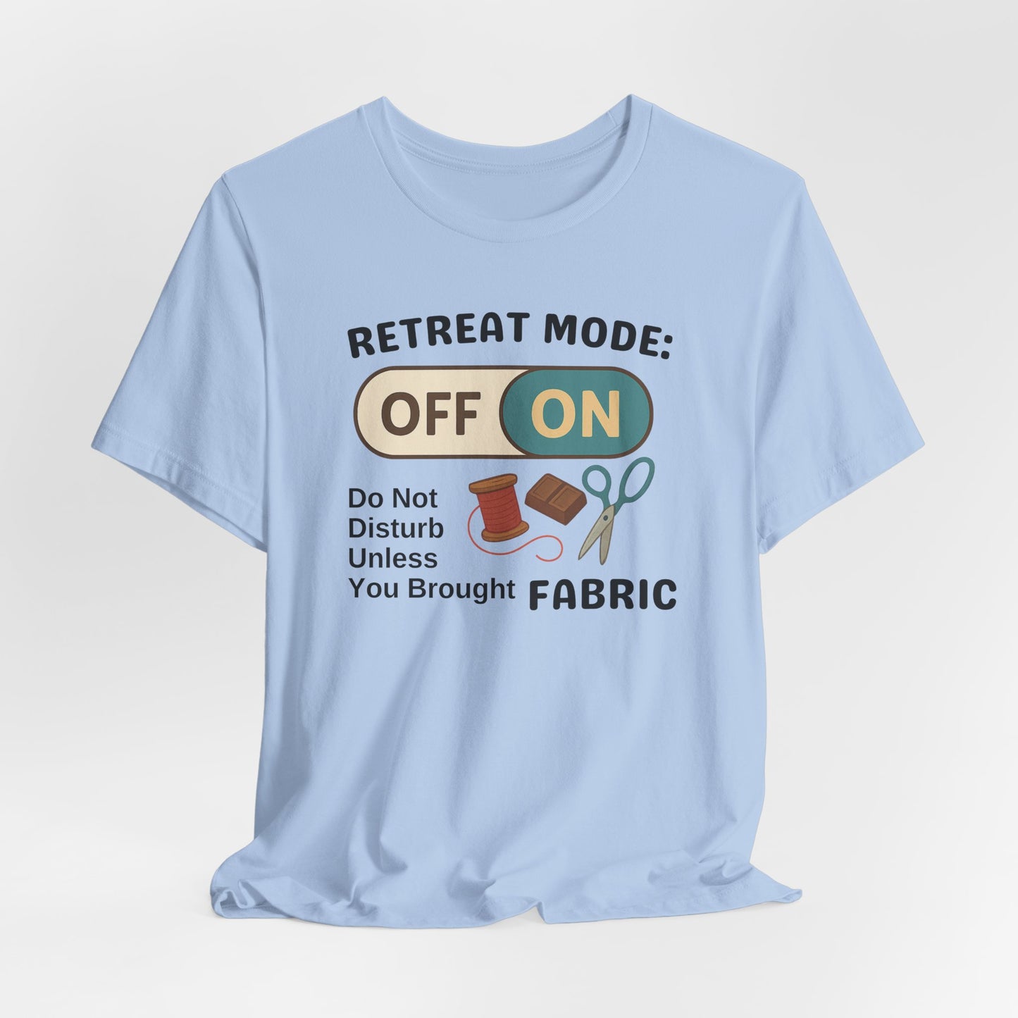 A A Baby Blue t-shirt with a toggle switch that says "Retreat Mode: OFF/ON" surrounded by a spool of thread, chocolate, and scissors. Text below reads "Do not disturb unless you brought fabric." Fun gift for quilting retreats.