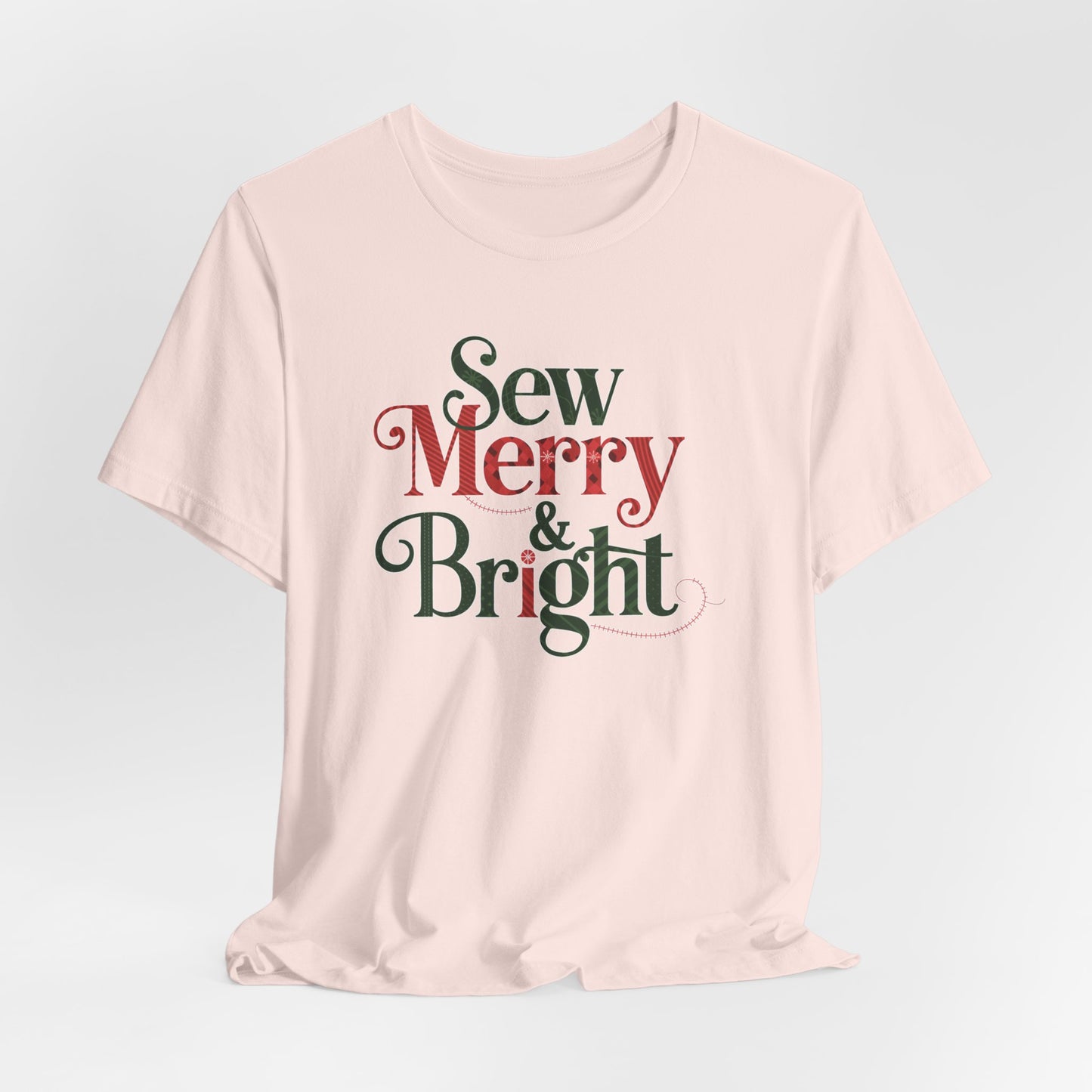 A Soft Pink t-shirt with the phrase "Sew Merry & Bright," incorporating sewing-inspired elements and holiday-themed accents, such as stitching lines and festive patterns.